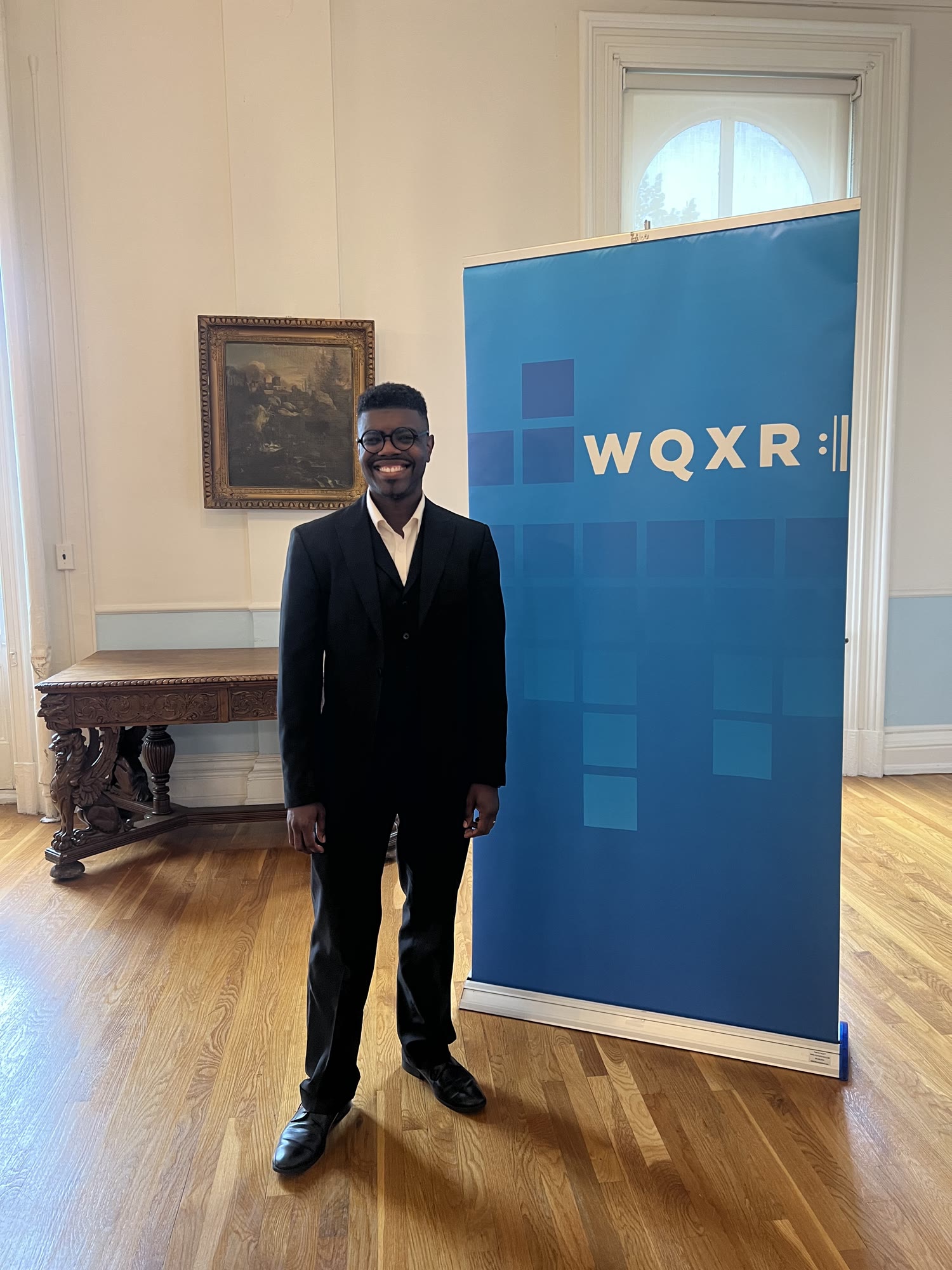 Kyle P. Walker standing beside a WQXR banner