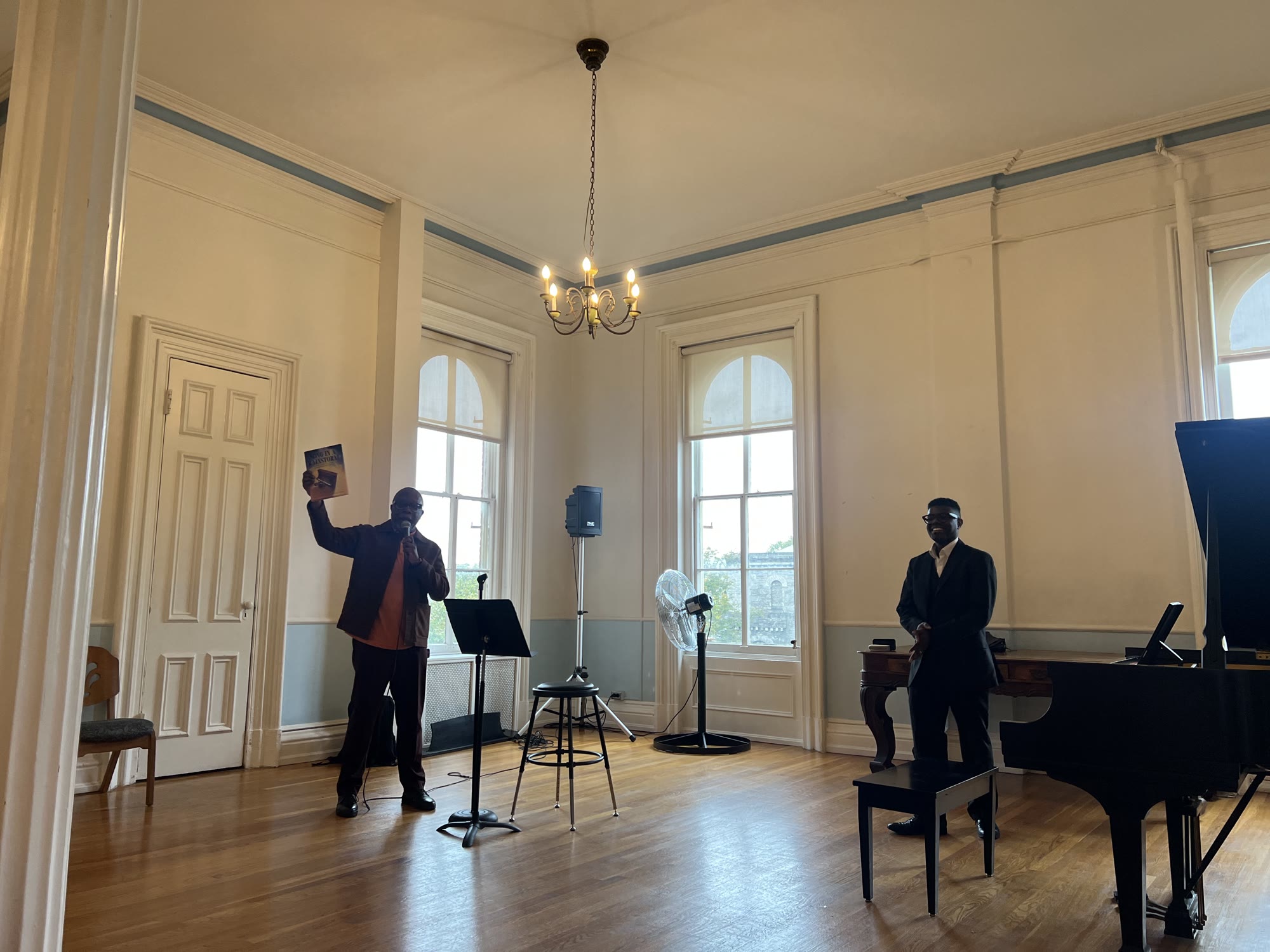 Ron Kavanaugh holding up Song in a Rainstorm while Kyle P. Walker stands at the piano